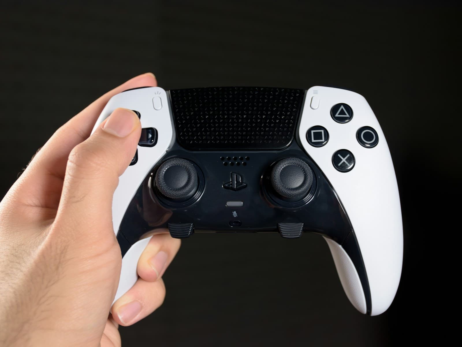 Une main tient une DualSense Edge blanche et noire, avec ses touches Fn sous les joysticks
