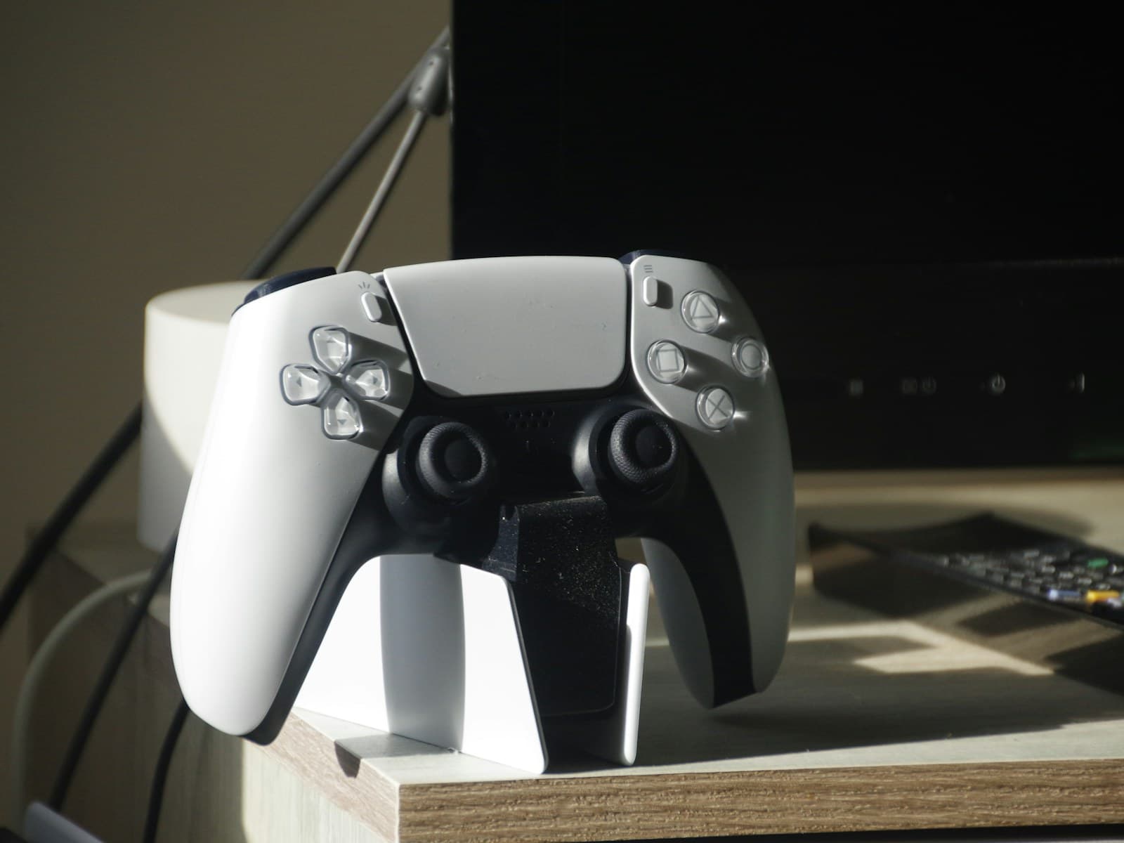 Une manette DualSense blanche posée sur un support de recharge, sur un bureau en bois